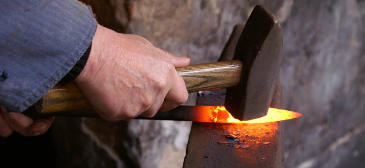Jemand schmiedet heißes Eisen mit einem Hammer